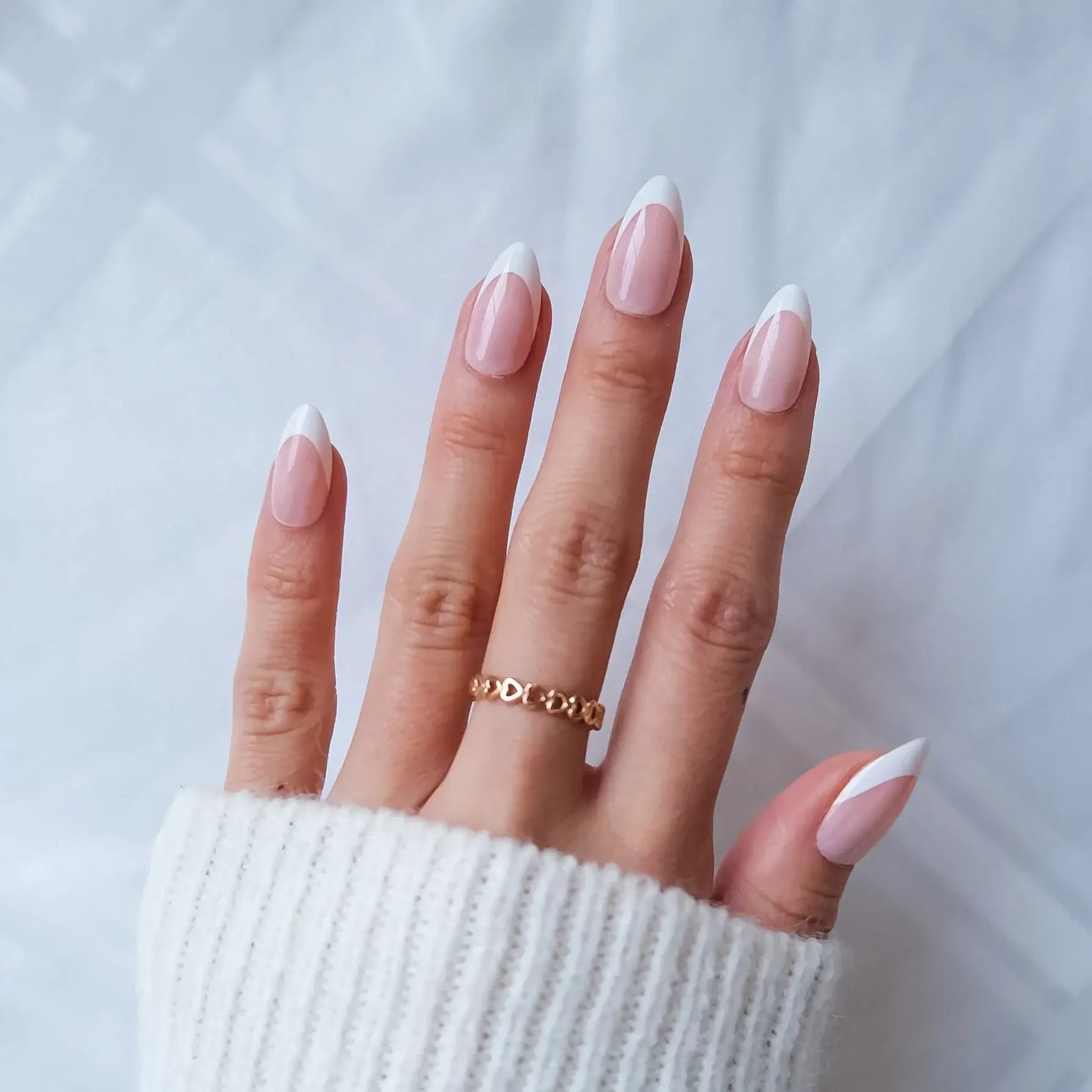 Hand with pink nail polish and a gold ring on a light background