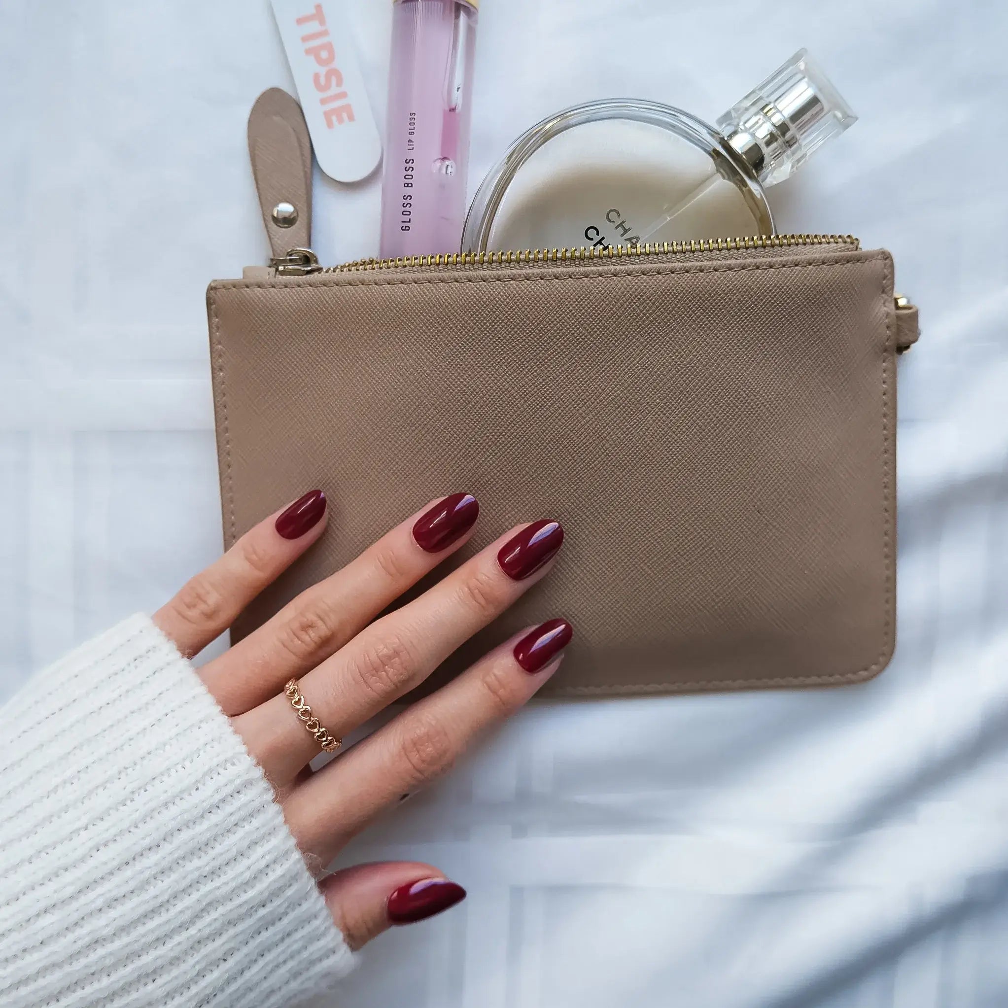 Beige pouch held by a hand with red nail polish, with a white background