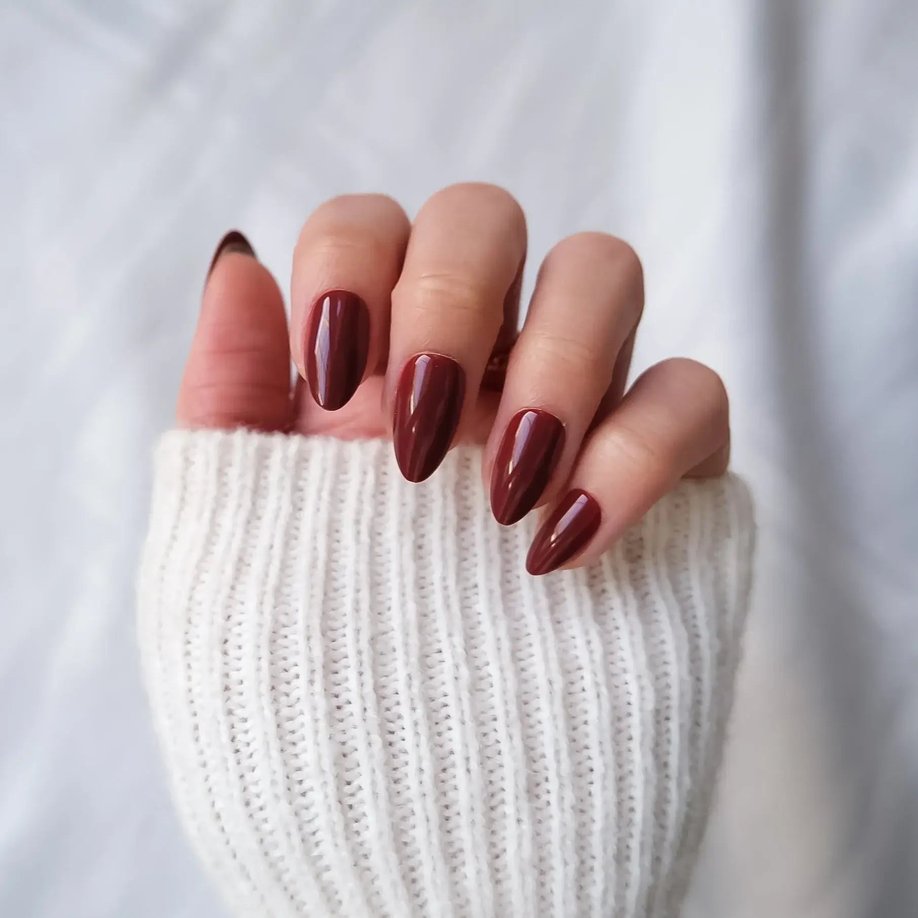 Close-up of a hand with dark red nail polish wearing a white knit sleeve.