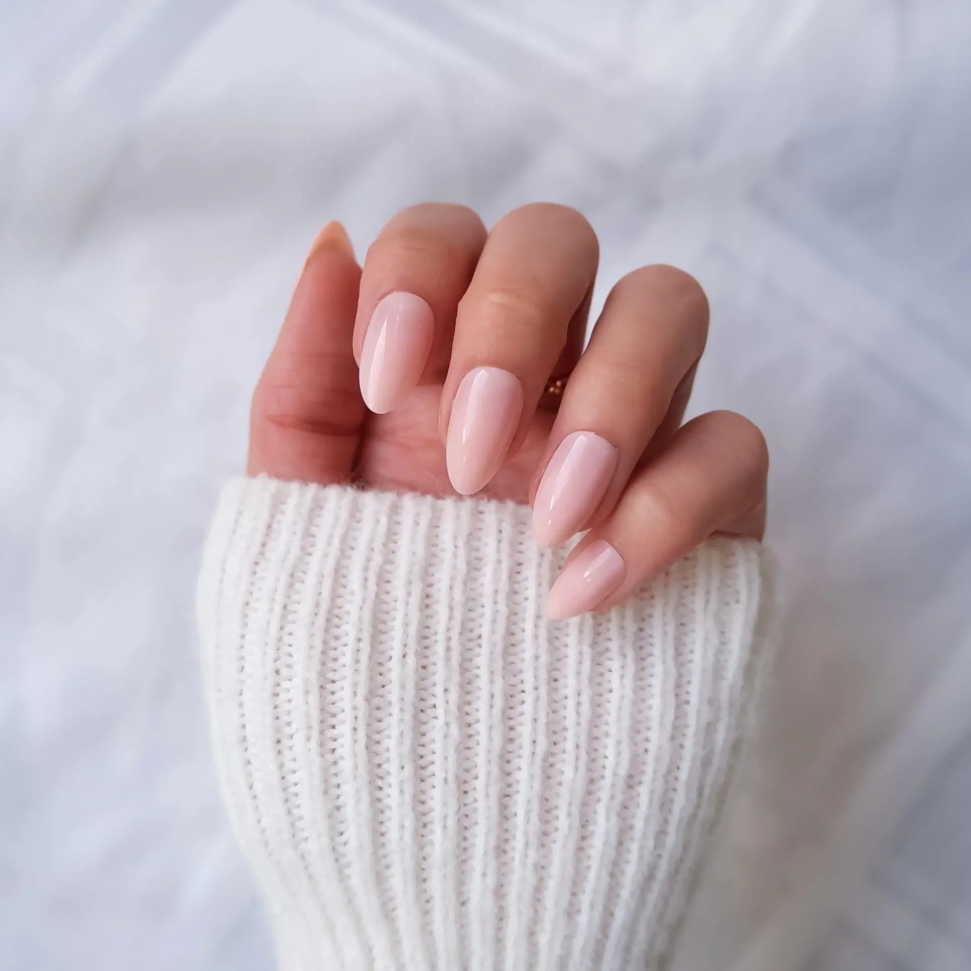 Close-up of a hand with pink nail polish wearing a white ribbed sweater.