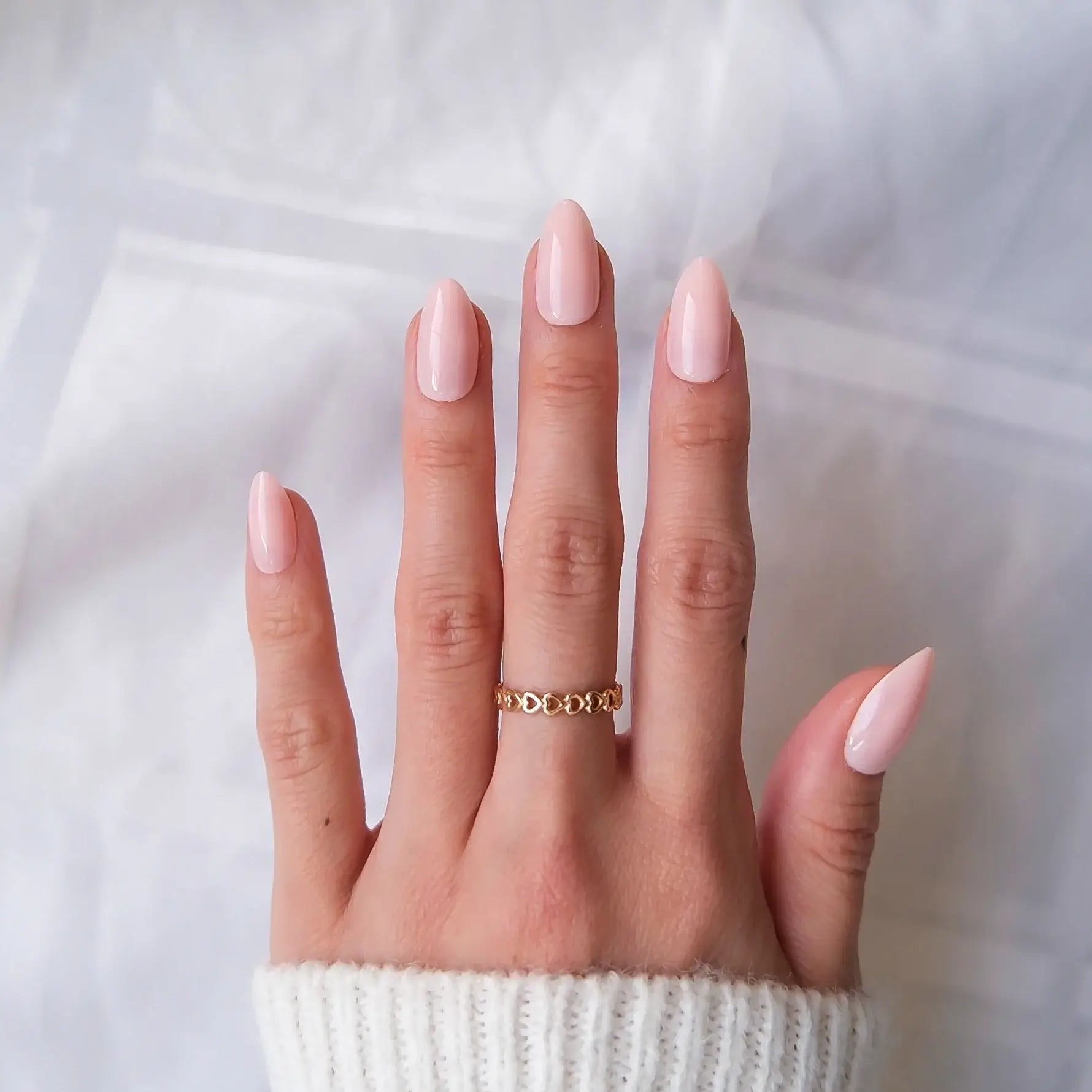 Hand with pink nail polish wearing a gold ring on a white background
