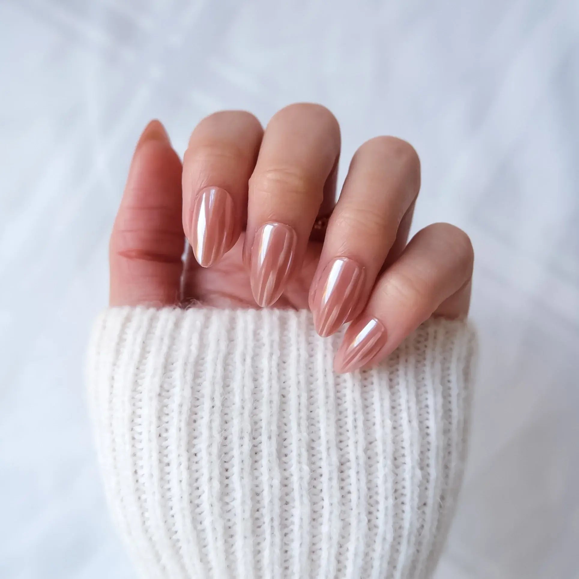 Hand with pink press-on nails wearing a white knit sleeve on a light background