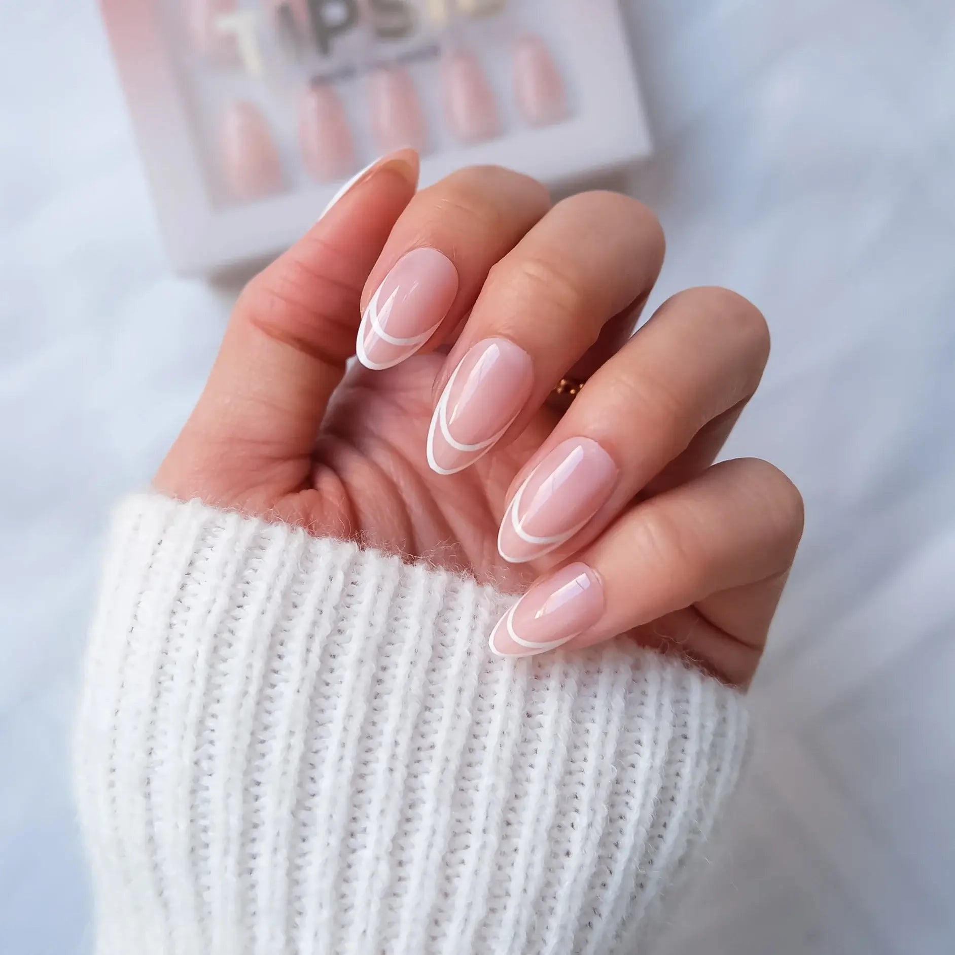 Hand with pink french tip press-on nail wearing a white sleeve against a blurred background