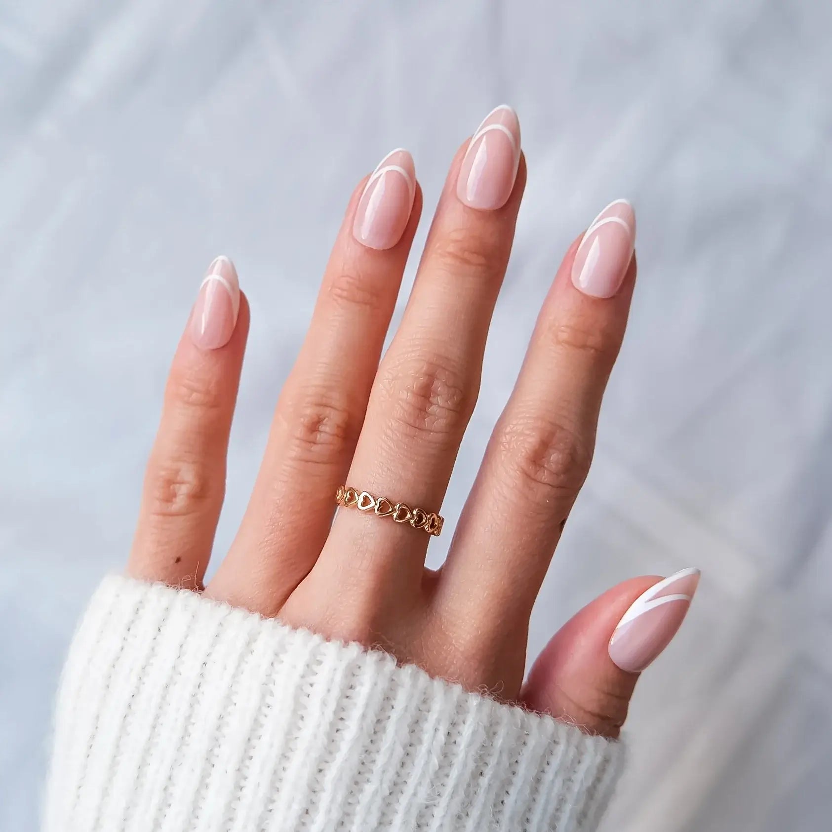 Hand with pink french tip press-on nails wearing a gold ring on a light gray background