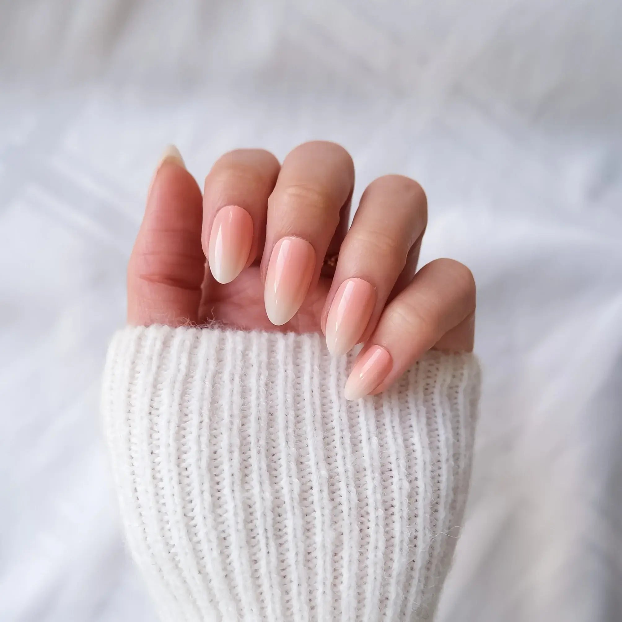 Close-up of a hand with peach to white gradient press-on nails wearing a white knit sleeve.