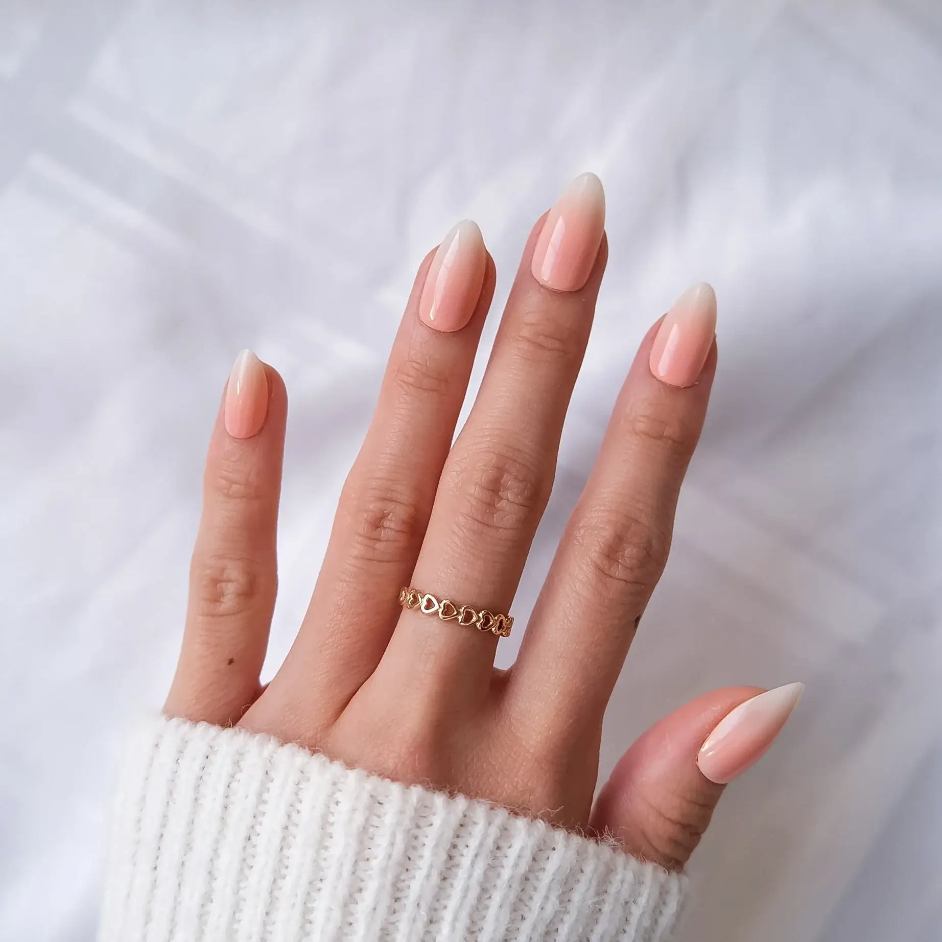Hand with peach to white press on nail wearing a gold ring on a white background