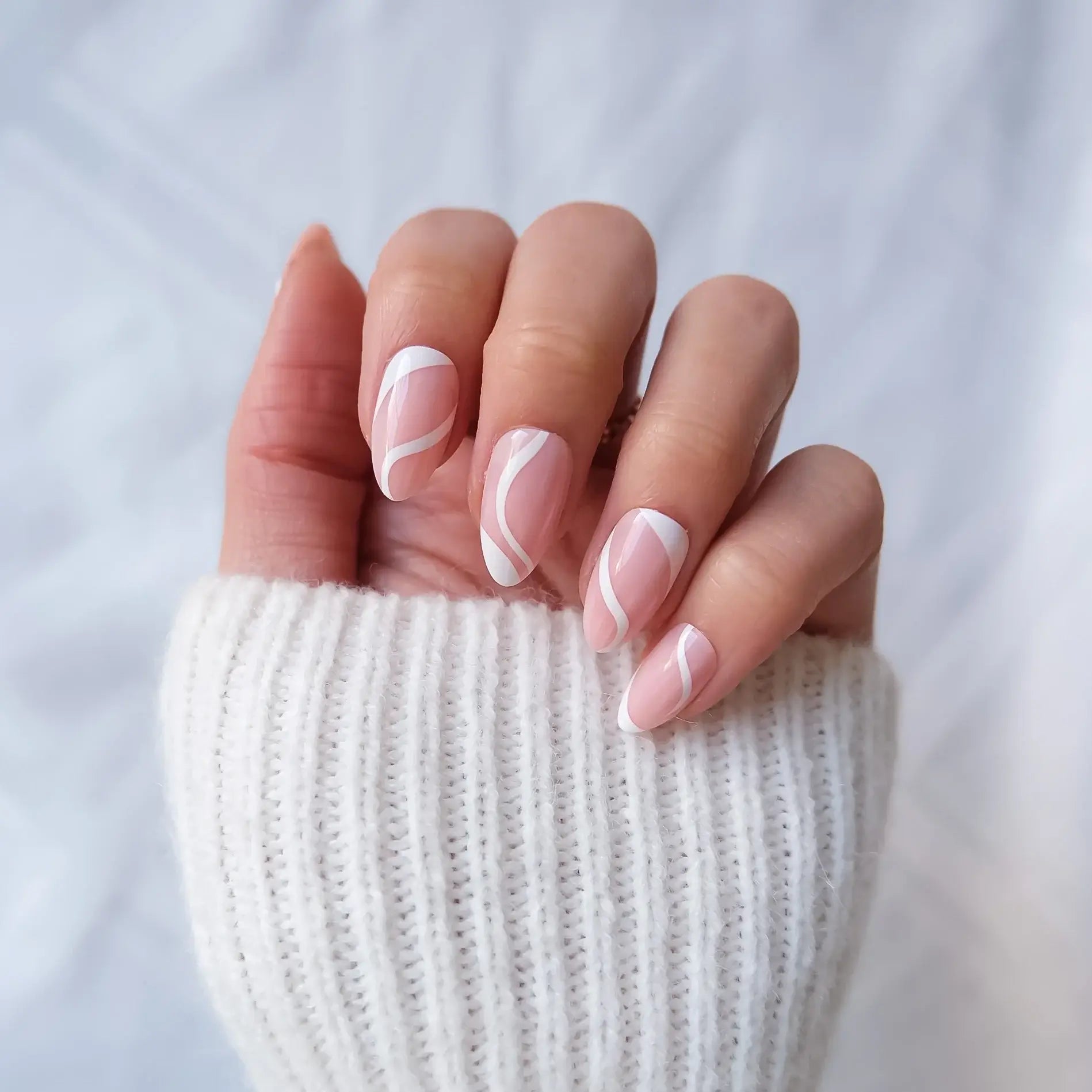 Hand with pink nail polish wearing a white sleeve against a light background
