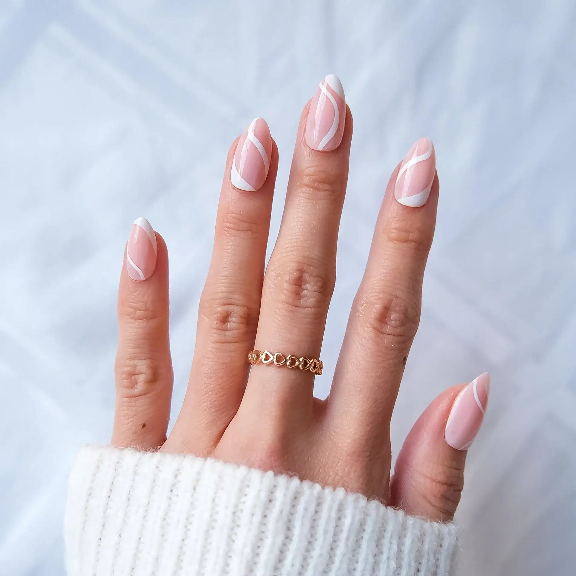 Hand with pink nail polish and a gold ring on a light background