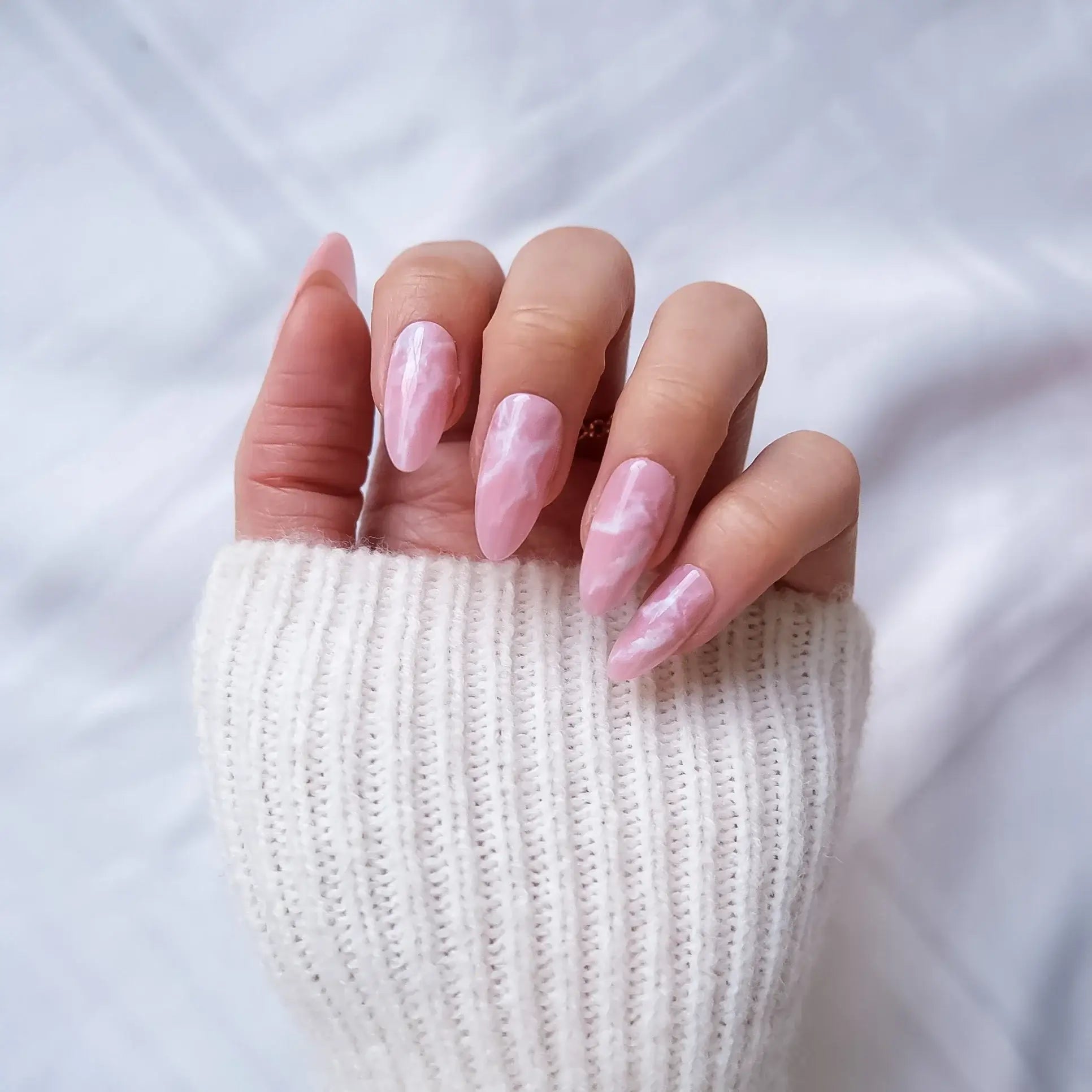 Hand with pink press-on nails wearing a white knit sleeve on a light background