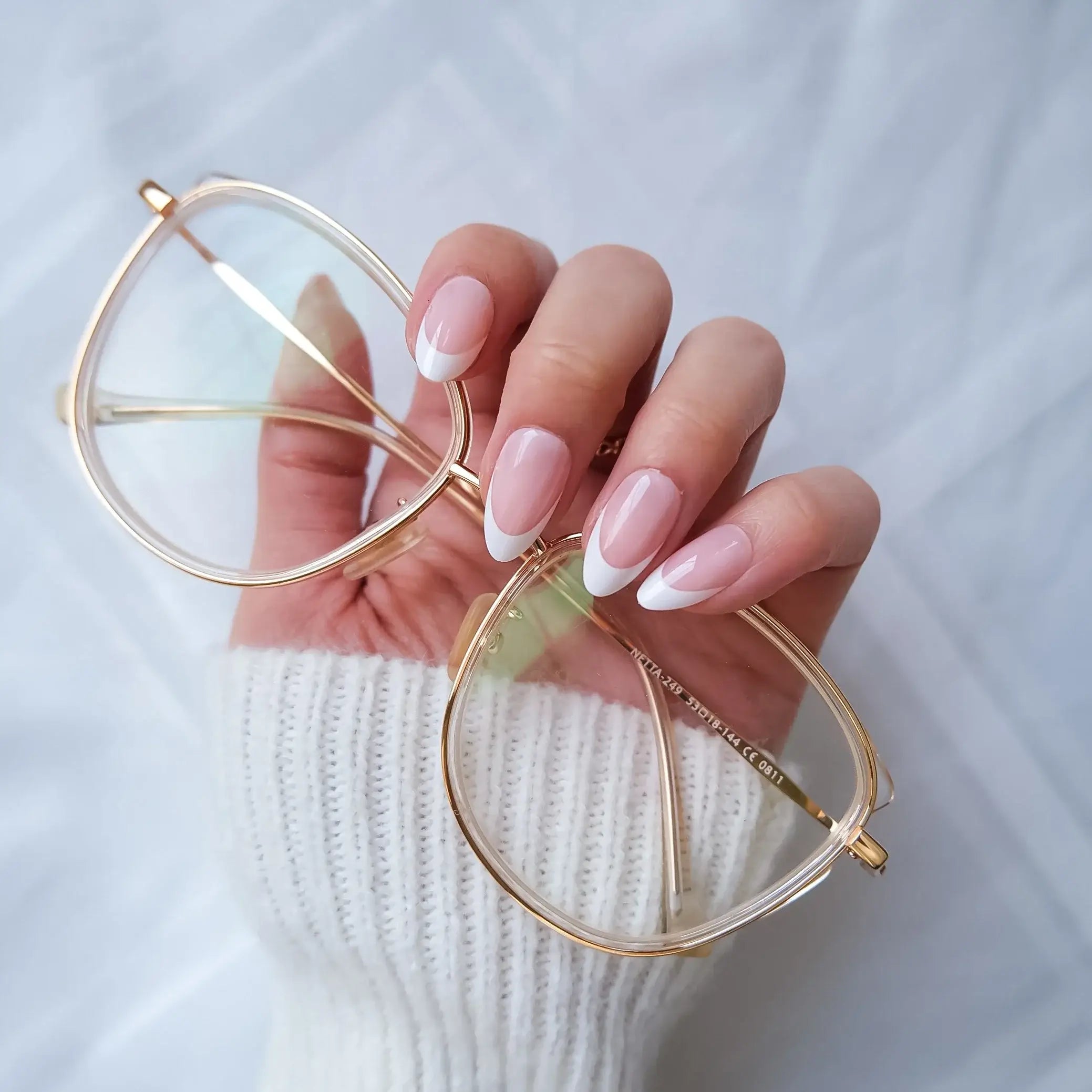 Hand with pink nail french tip press on nails behind a white textured fabric