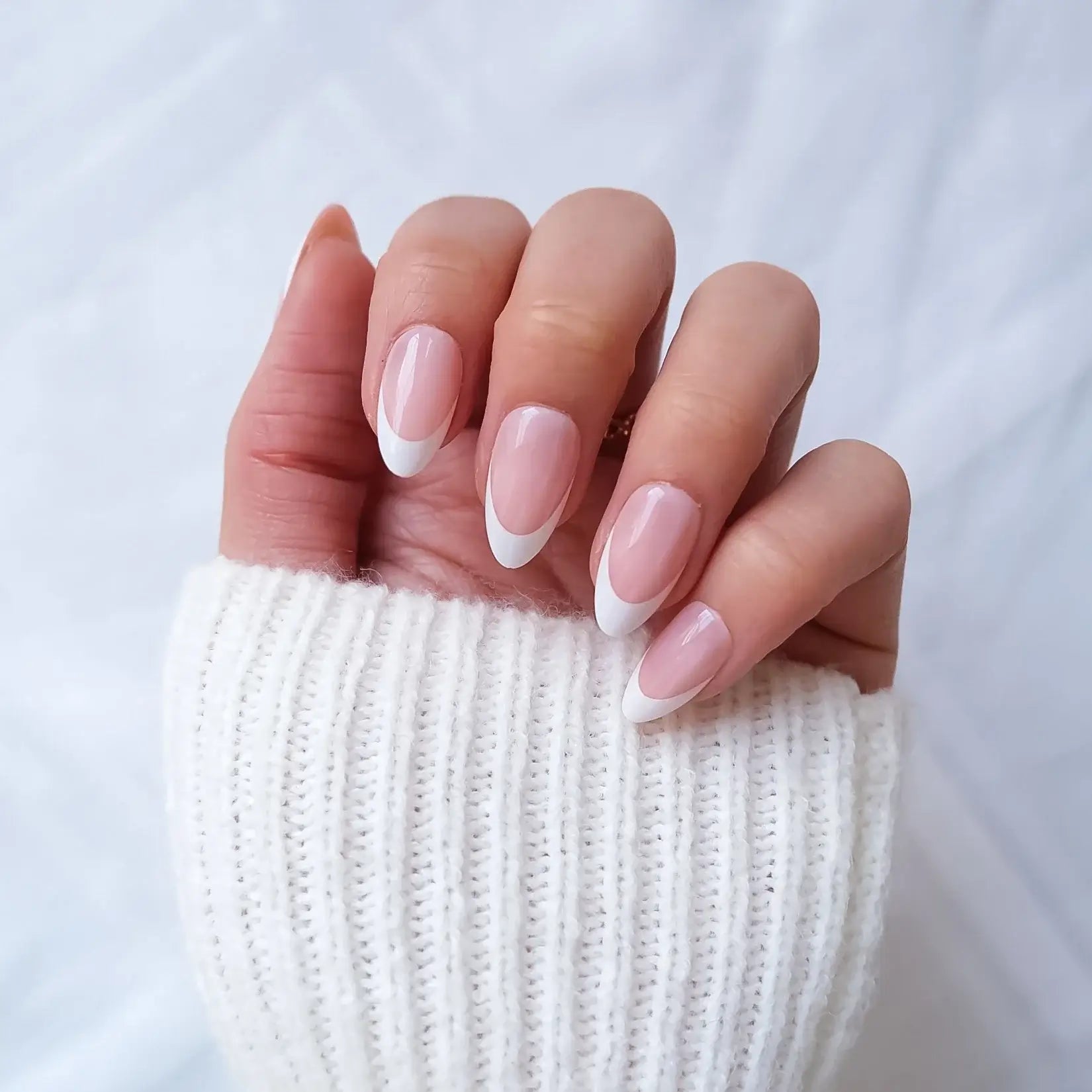 Hand with pink and white nail polish wearing a rose gold ring on a textured white background