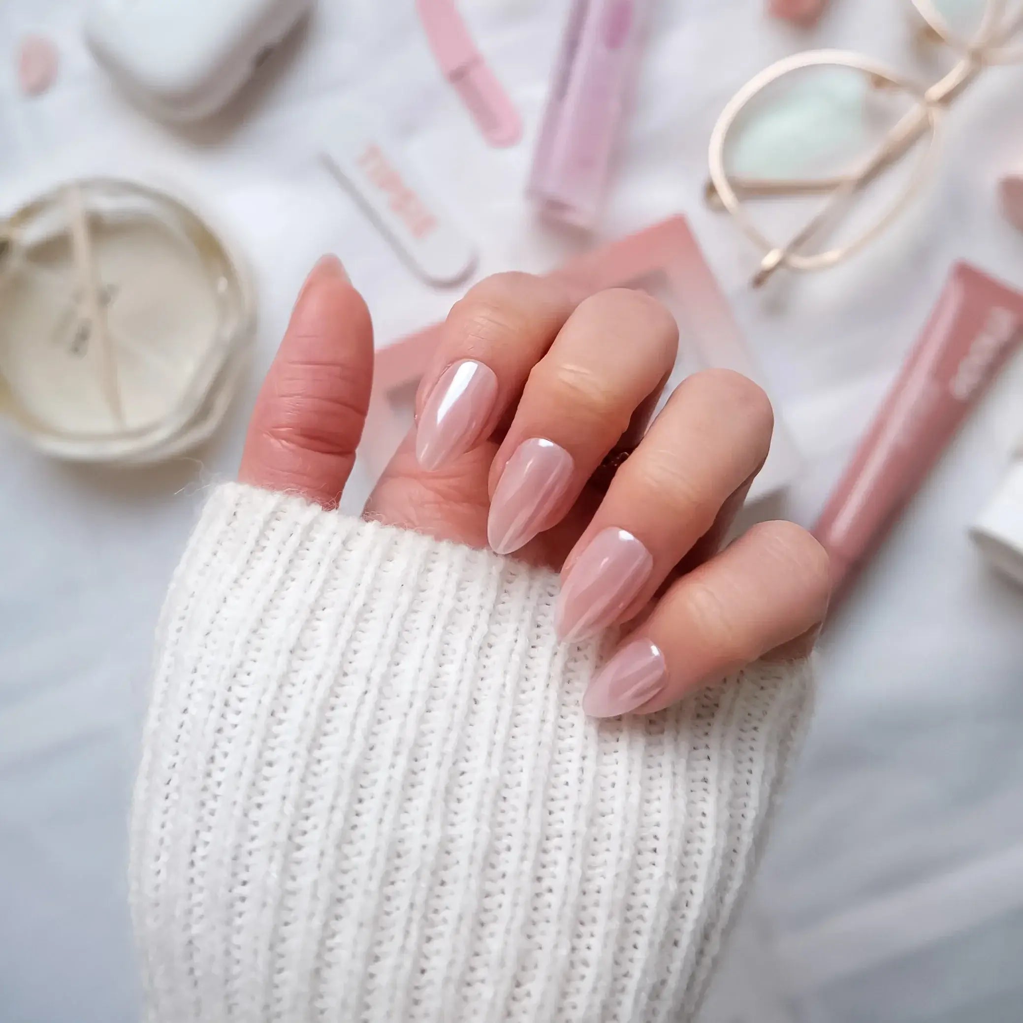 Hand with light pink nail press-on nails on a textured white background