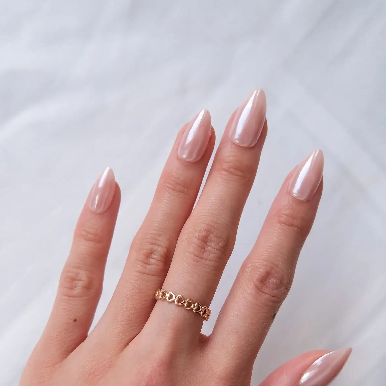 Hand with pink nail polish and a gold ring on a white fluffy surface