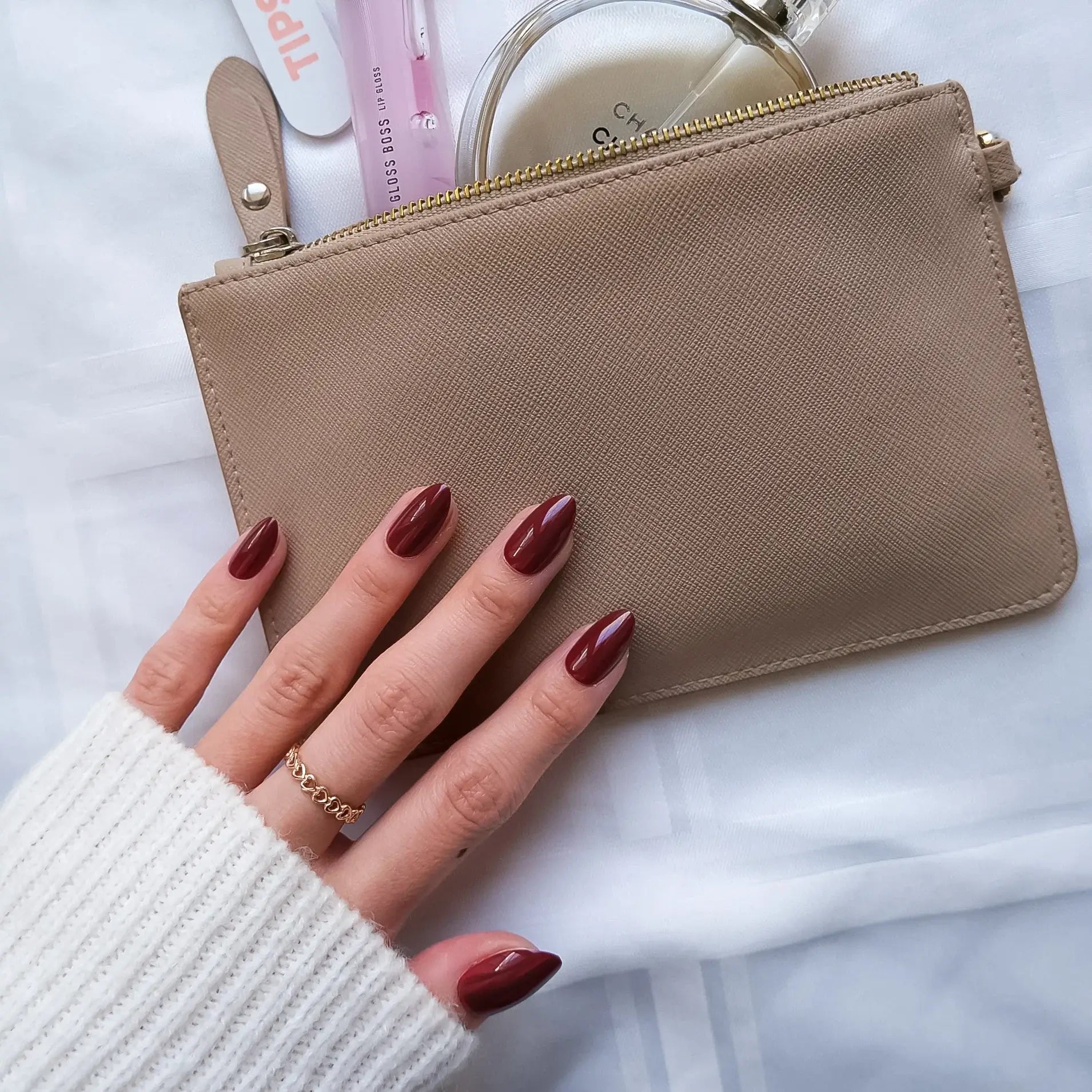 Beige wallet held by a hand with red nail polish on a white background