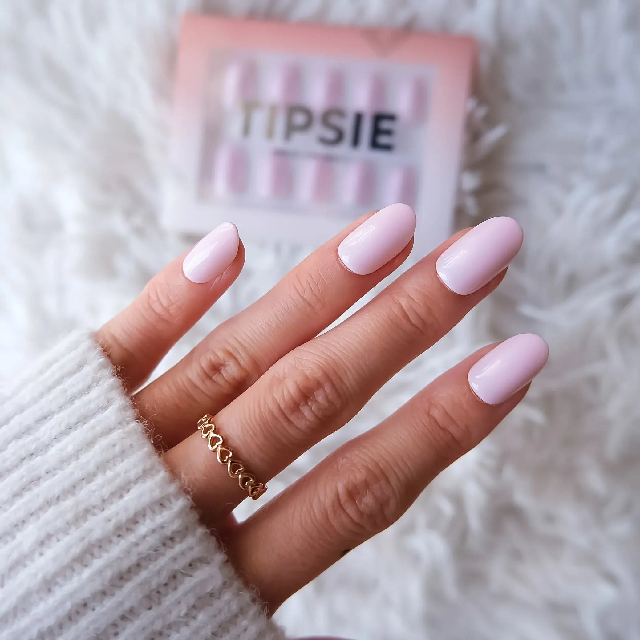 Hand with pink nail press-on nails with a pink 'TIPSIE' box on a white fluffy background