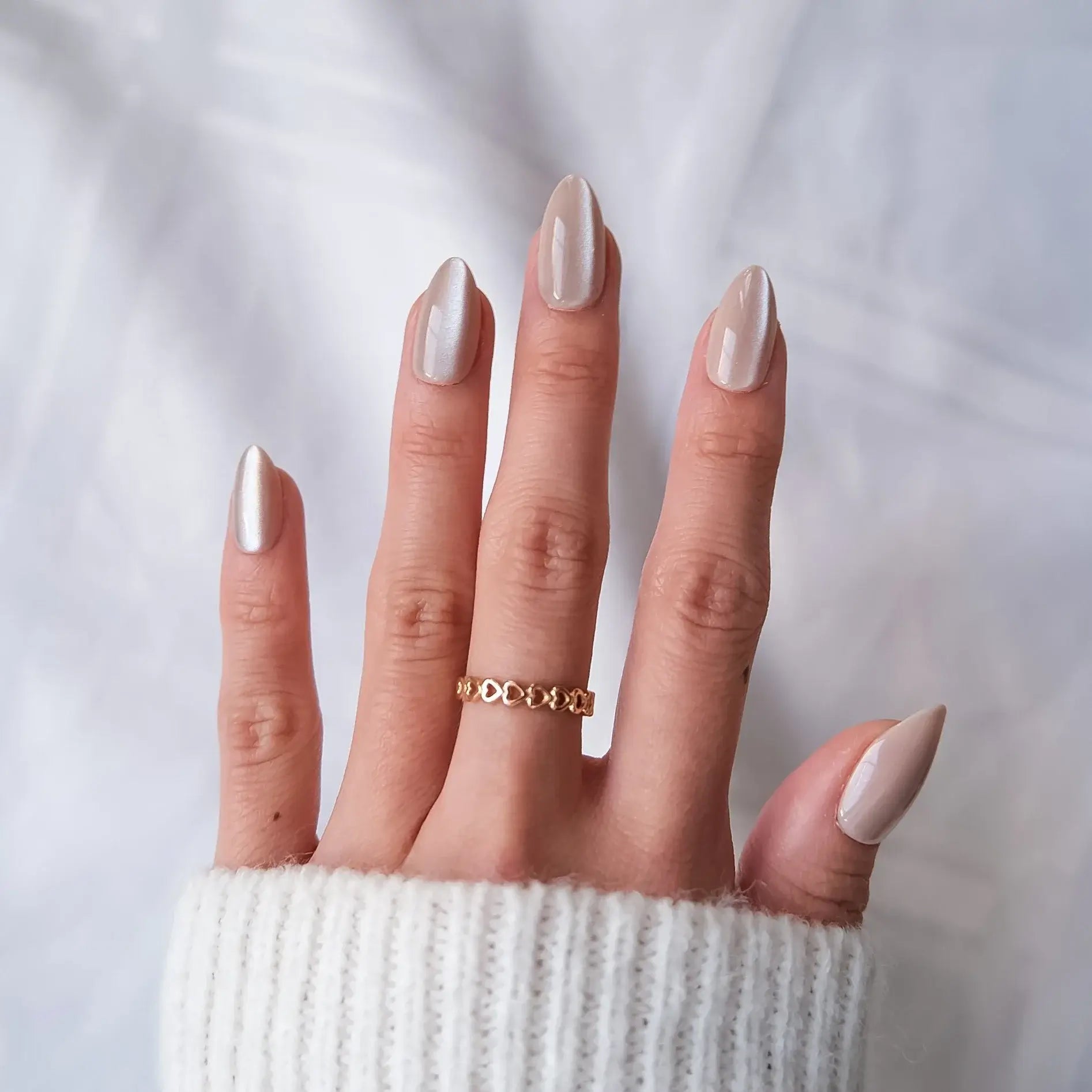 Hand with sparkly press-on nails wearing a gold ring on a light background